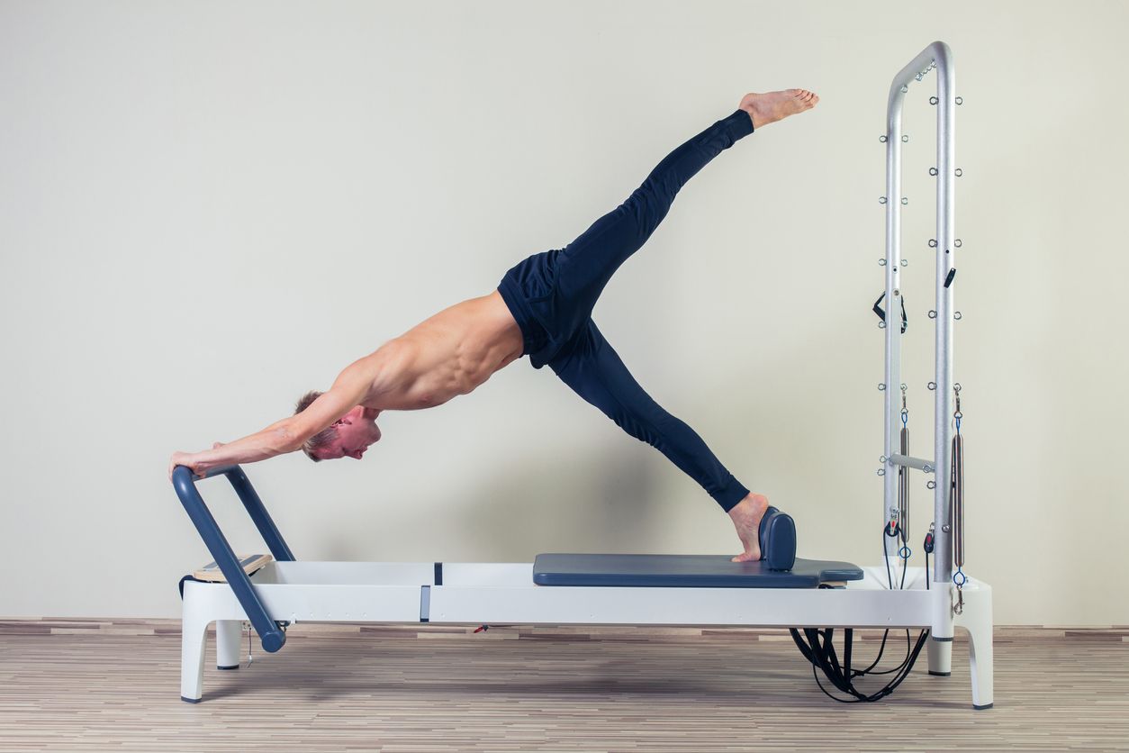 Pilates reformer workout exercises man at gym indoor.